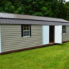 A spacious 12x32 Frontier Garage Shed with a metal roof stands on a grassy field. It features windows and an open white door, providing a glimpse of the interior, while trees can be seen in the background.