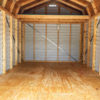 Interior of an empty 12x32 Frontier Garage Shed featuring visible framing. The floor and walls are constructed from light wood, while the vaulted ceiling showcases exposed beams. Natural light streams in through small openings at the top, accentuating the spacious and unfinished interior.