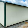 A 10x20 Ridgeline Shed, featuring a beige exterior with dark green trim, is positioned on a gravel lot. The shed showcases a sloped roof and has one side without any windows facing the viewer. The sky above is partly cloudy, with some greenery visible in the background.