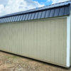 A 12x24 Frontier Garage Shed in beige with a black metal roof is situated on a gravel lot beneath a partly cloudy sky.