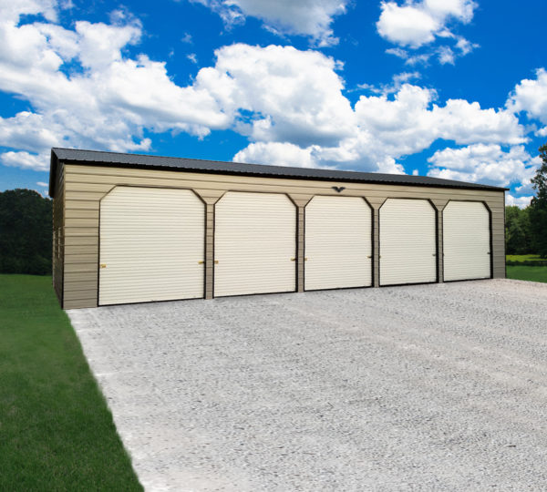 The 24x60x12 5-Bay Garage, made of metal and featuring five closed doors, stands on a gravel driveway. The surrounding area is grassy, under a clear blue sky with scattered clouds above.