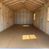 Interior of an empty 12x28 Ridgeline Garage with exposed beams, panel walls, two right windows, rear door, sunlight casting shadows.