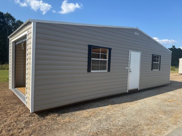 12x20 storage garage shed with light gray metal exterior, white door, two black-trimmed windows, open bay on dry grass under clouds.