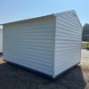 The 10x12 Ridgeline Shed #062541366 with a white metal exterior and sloped roof sits on dry grass near pavement, trees, and sheds.