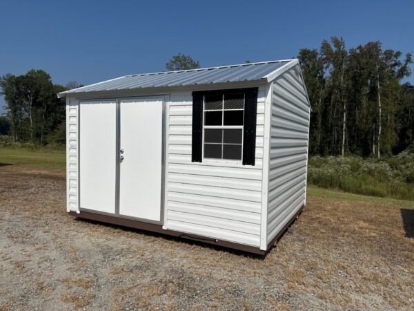 The 10x12 Ridgeline Shed #041138462 is a small white metal unit with double doors, window, on dry grass with trees behind.