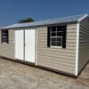 The 12x16 Ridgeline Shed #041138463 has beige metal siding, white double doors, and two windows with black shutters on gravel.