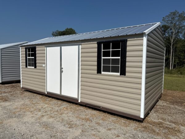 The 12x16 Ridgeline Shed #041138463 has beige metal siding, white double doors, and two windows with black shutters on gravel.
