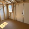 Interior of 10x12 Ridgeline Shed #041138462 with exposed wood framing, metal walls and roof, sunlit window, closed white door, bare floor.