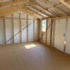 Interior of a 12x16 Ridgeline Shed with unfinished wooden framing, metal walls and ceiling, sunlight through window, white door right.