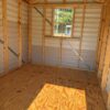 The 8x10 Ridgeline Shed #071538877 has unfinished plywood flooring, wood framing, metal walls, a window, and sunlight patterns inside.