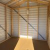 Sunlight streams into the empty 8x8 Ridgeline Shed, showing metal walls, roof, exposed framing, and a small sign. Available now.