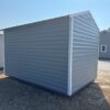 The 8x12 Ridgeline Shed #022041155 with gray metal siding and white-trimmed roof sits on dry grass near a road, under blue sky.