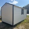 8x16 Ridgeline Shed (Stock #112740290), white exterior, black frame, window, on grass and gravel, sunny sky, trees behind.