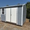 The 8x12 Ridgeline Shed #022041155 has a metal roof, double doors, and a side window. Gray and white on dry grass below blue sky.