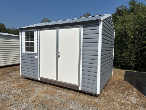 The 8x12 Ridgeline Shed #022041155 has a metal roof, double doors, and a side window. Gray and white on dry grass below blue sky.