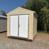 The 8x8 Ridgeline Shed (#082541439), a beige metal shed with white double doors and sloped roof, stands on dry grass and gravel.