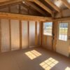 Interior of the 12x16 Frontier Shed features unfinished wood, exposed beams, insulation, and sunlight casting shadows on the floor.