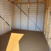 The interior of an empty 8x8 Ridgeline Shed with metal siding, exposed framing, brown floor, and sunlight streaming through the door.