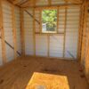Interior of the 8x10 Scratch and Dent Ridgeline Shed, empty with exposed framing, plywood floor, metal walls, and one sunlit window.