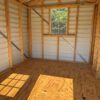 Interior of empty 8x10 Ridgeline Shed with light plywood floor, metal siding, exposed framing, sunny window, and shadow on floor.