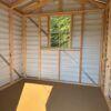 The interior of the 8x8 Ridgeline Shed (#082541439) has light metal walls, exposed wooden framing, a sunlit window, and plywood floor.