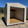 The 10x14 Estate Garage Shed features a beige metal exterior, open garage door, unfinished wood inside, on grass with trees behind.