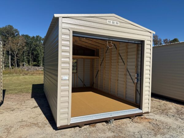 The 10x14 Estate Garage Shed features a beige metal exterior, open garage door, unfinished wood inside, on grass with trees behind.