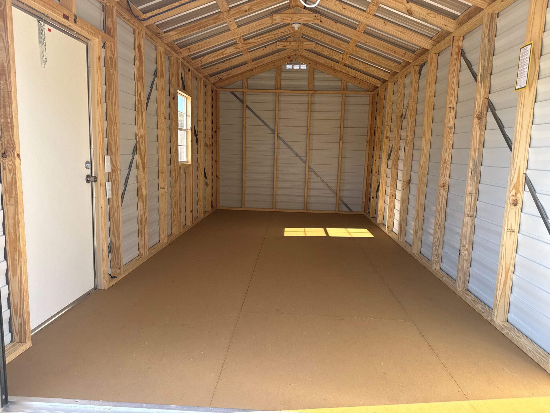 Interior of 10x20 Ridgeline Garage Shed with wood framing, white metal door left, two windows, and sunlight on brown floor.