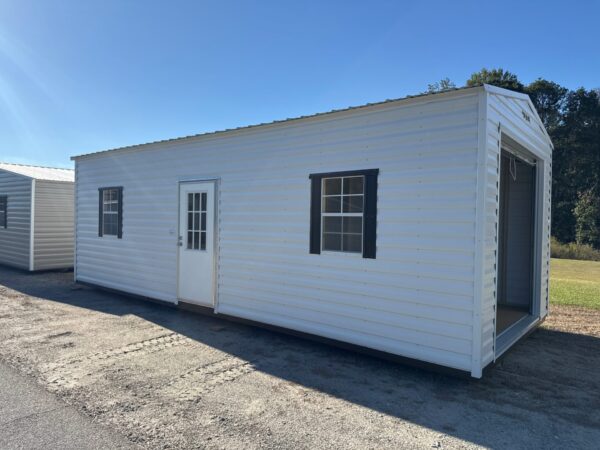 A 10x20 Ridgeline Garage Shed, stock #082541441, with door, three windows, garage entrance, on gravel lot under blue sky.