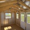 The 10x16 Frontier Shed has an unfinished wood interior, exposed framing, three windows, and double doors. Sunlight highlights wood.