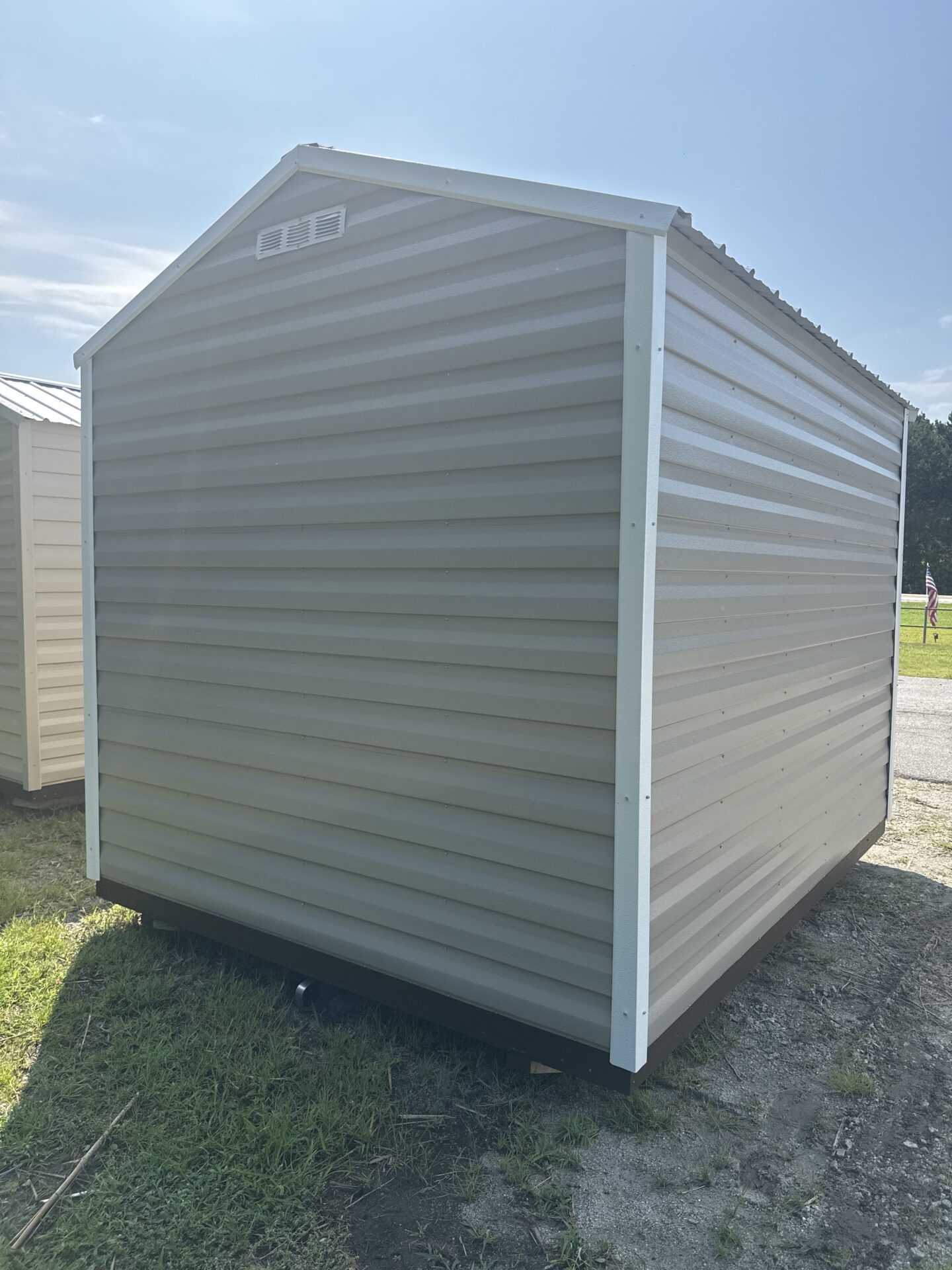 8x10 Ridgeline Shed (Stock #041341716), light gray with white trim, on grass and gravel under a sunny sky; no doors or windows visible.