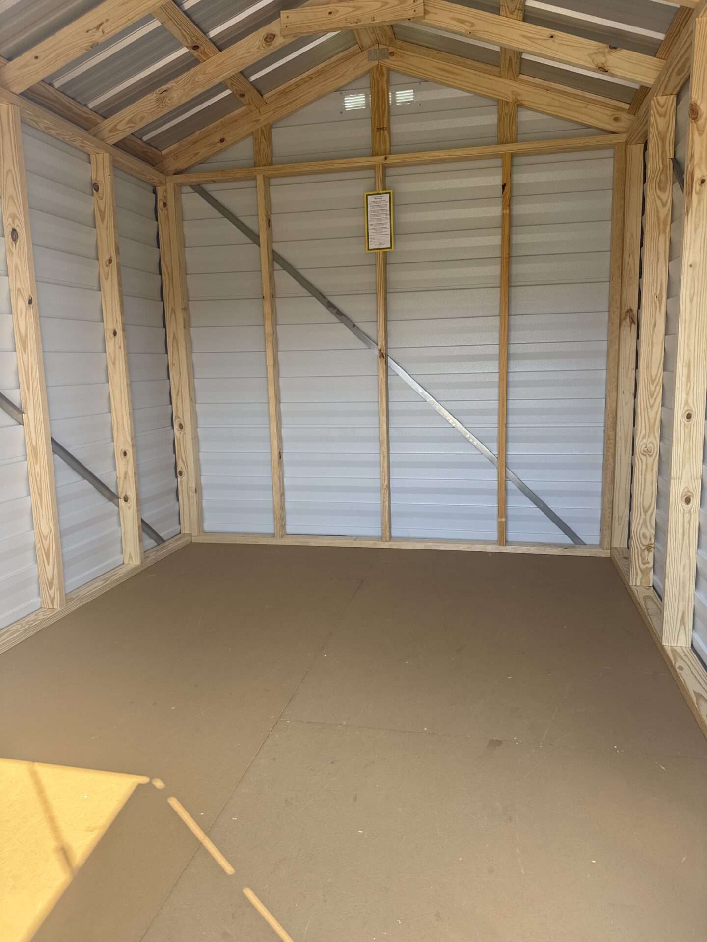 Interior of 8x10 Ridgeline Shed, exposed wood framing, metal wall panels, brown floor, rear window with sunlight. Available now.