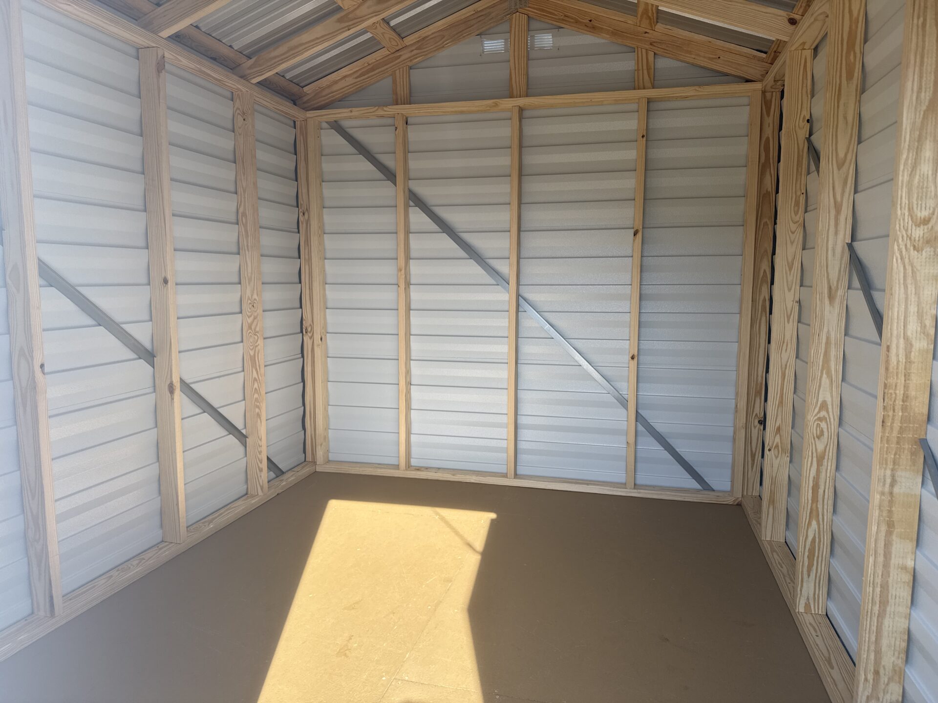 Interior of an empty 8x10 Ridgeline Shed (Stock #041341716) featuring exposed framing, metal wall panels, and sunlight streaming onto the floor.