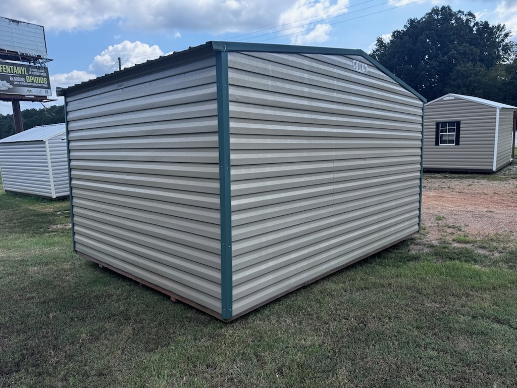 A 12x16 Storage Garage Shed - Scratch & Dent - Stock #0622EP30538 in light gray with green trim is situated on a grassy area, with another similar shed and trees visible in the background beneath a partly cloudy sky.